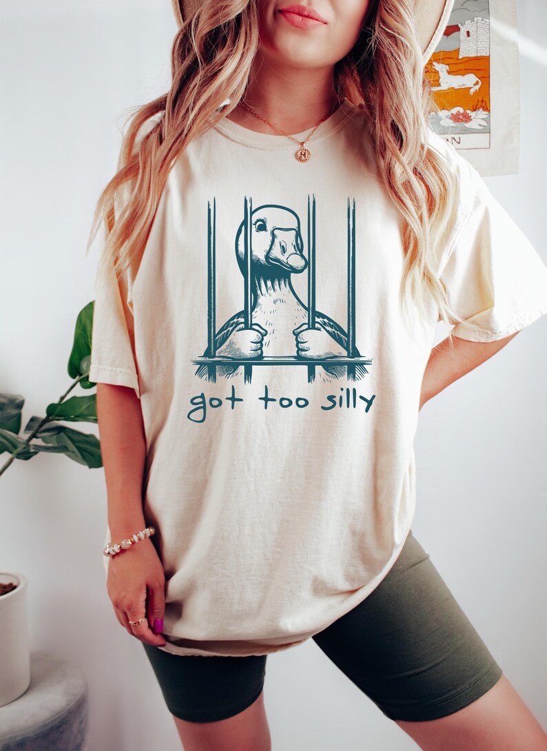 May include: A white t-shirt with a graphic of a goose in a cage. The text "got too silly" is printed below the graphic.