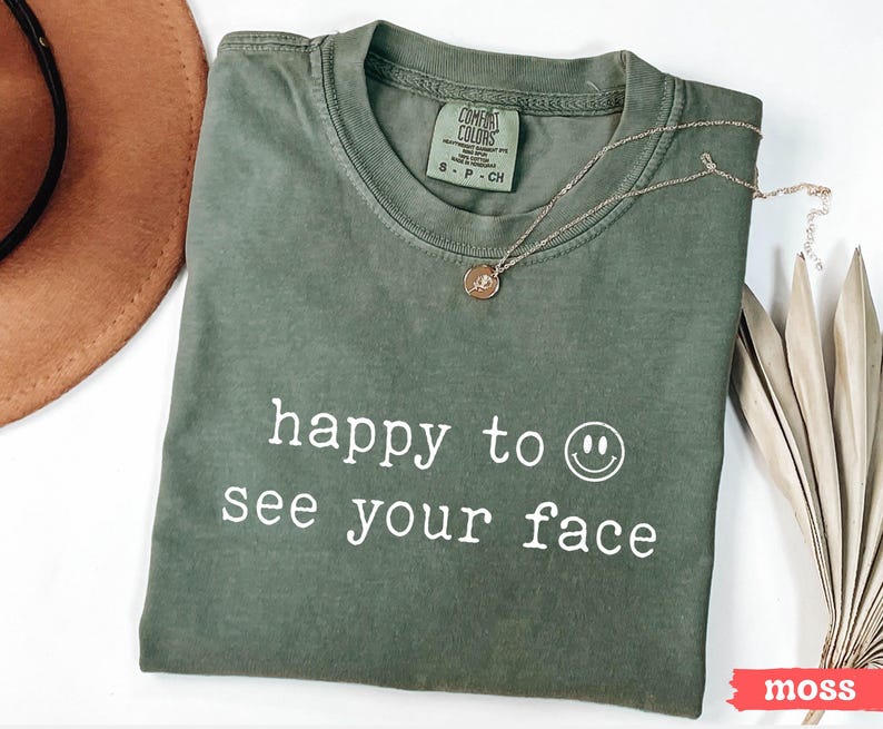 May include: A green t-shirt with the text "happy to see your face" and a smiley face graphic printed in white.
