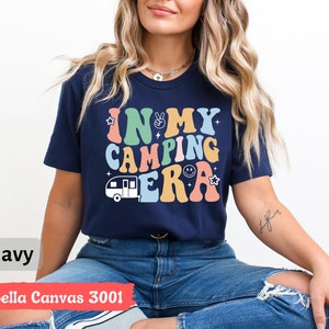 May include: A navy blue Bella Canvas 3001 t-shirt with the text "In My Camping Era" in rainbow colors and a cartoon camper van graphic.