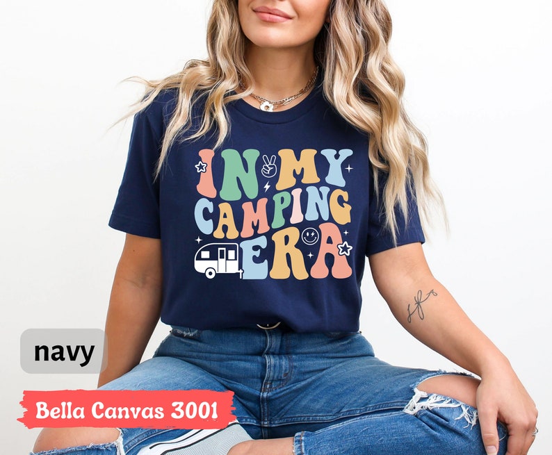 May include: A navy blue Bella Canvas 3001 t-shirt with the text "In My Camping Era" in rainbow colors and a cartoon camper van graphic.