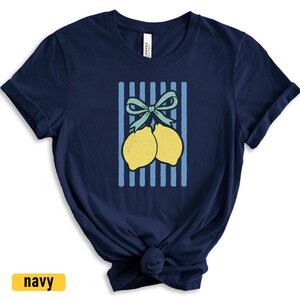 May include: A navy blue t-shirt with a graphic of two lemons tied together with a green bow on a blue and white striped background.