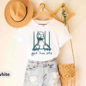 May include: White t-shirt with a graphic of a duck in a cage and the text "got too silly".