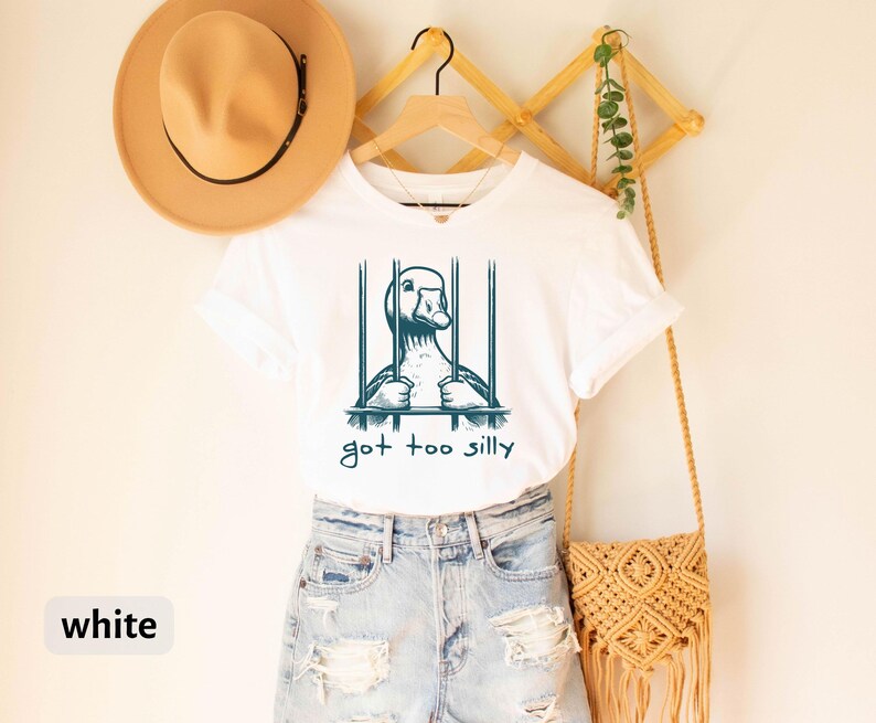 May include: White t-shirt with a graphic of a duck in a cage and the text "got too silly".