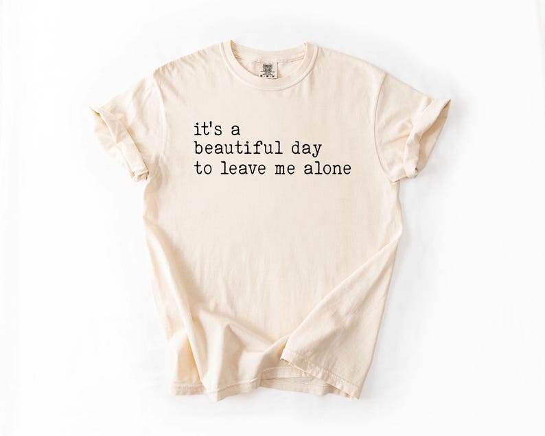 May include: A beige t-shirt with the text "it's a beautiful day to leave me alone" printed in black.