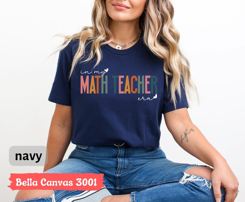 May include: A navy blue t-shirt with the text "in my math teacher era" in rainbow colours. The shirt is made by Bella Canvas and is a 3001 style.