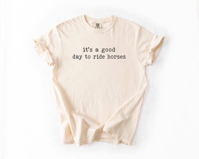 May include: A beige t-shirt with the text "it's a good day to ride horses" printed in black.