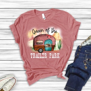 May include: A pink t-shirt with the text "Queen of the Trailer Park" and a cartoon image of a camper van in a desert landscape.