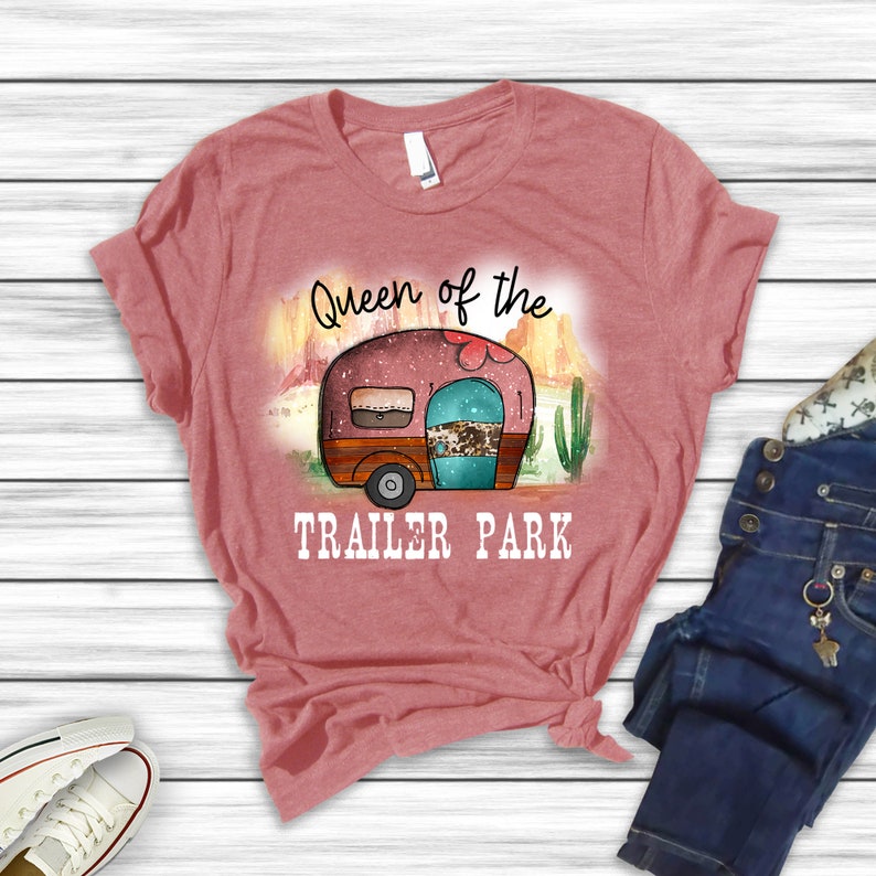 May include: A pink t-shirt with the text "Queen of the Trailer Park" and a cartoon image of a camper van in a desert landscape.