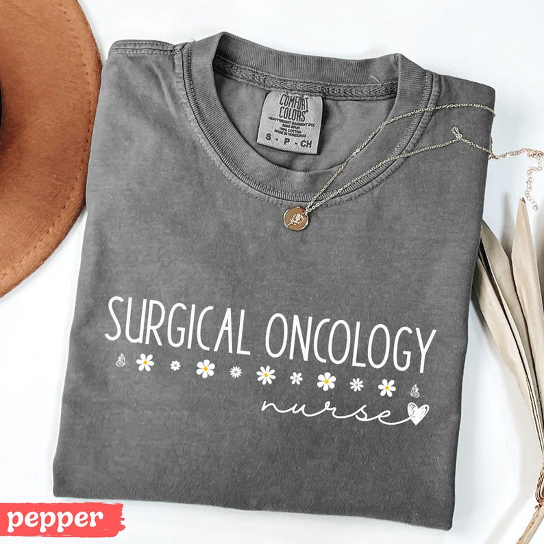 May include: A gray t-shirt with the text "SURGICAL ONCOLOGY nurse" in white lettering. The shirt has a small heart and daisy accents.