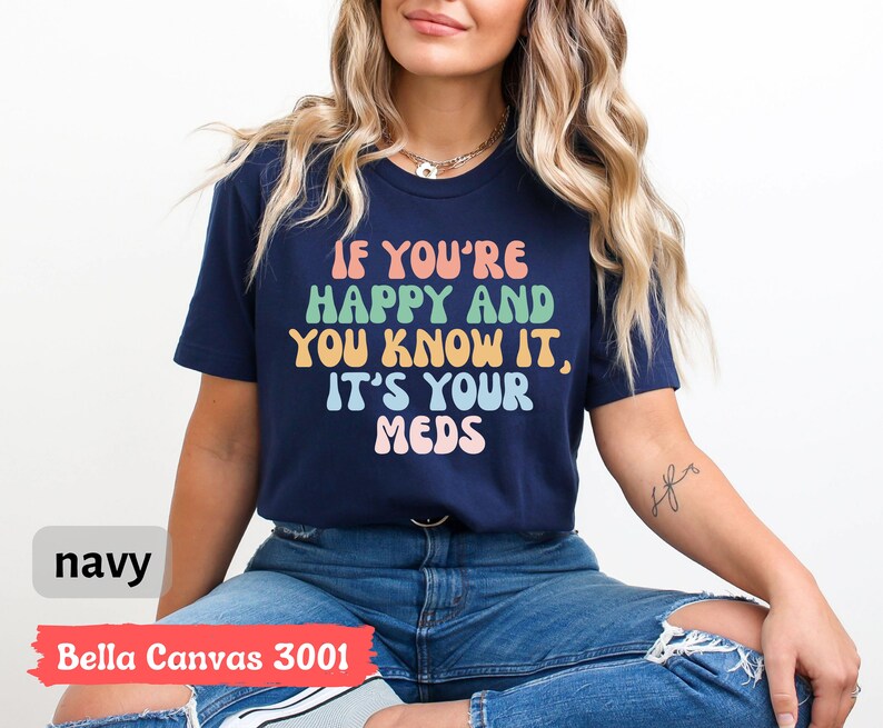 May include: A navy blue t-shirt with the text "If you're happy and you know it, it's your meds" in rainbow colors. The shirt is made by Bella Canvas and is a size 3001.