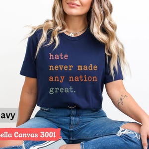 Op de afbeelding: Een marineblauw Bella Canvas 3001 T-shirt met de tekst "hate never made any nation great." gedrukt in regenboogkleuren.