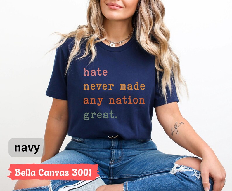 Op de afbeelding: Een marineblauw Bella Canvas 3001 T-shirt met de tekst "hate never made any nation great." gedrukt in regenboogkleuren.