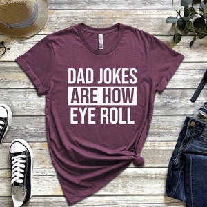 May include: A maroon t-shirt with white text that reads "Dad Jokes Are How Eye Roll".