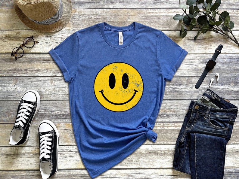 May include: A blue t-shirt featuring a yellow smiley face graphic. The smiley face has a distressed, vintage look.