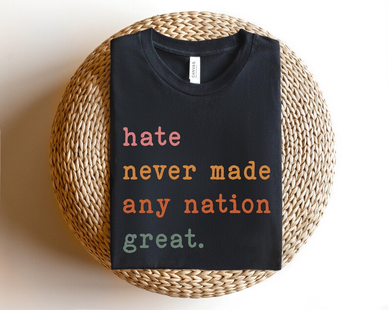 Op de afbeelding: Zwart T-shirt met de tekst "hate never made any nation great." gedrukt in oranje, roze en groen.