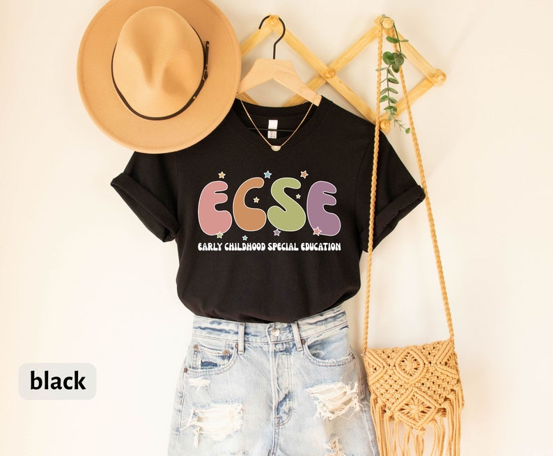 K&ouml;nnte beinhalten: Schwarzes T-Shirt mit dem Text "ECSE" in bunten Buchstaben, steht f&uuml;r "Early Childhood Special Education". Das Shirt h&auml;ngt an einem Holzgestell mit einem Strohhut und einer kleinen gewebten Tasche.