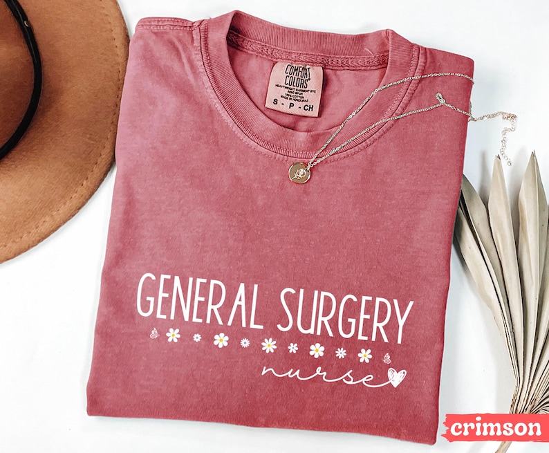 Może przedstawiać: Czerwony t-shirt z napisem "GENERAL SURGERY nurse" w białym kolorze. Koszulka ma małe białe serce i akcenty w postaci stokrotek.
