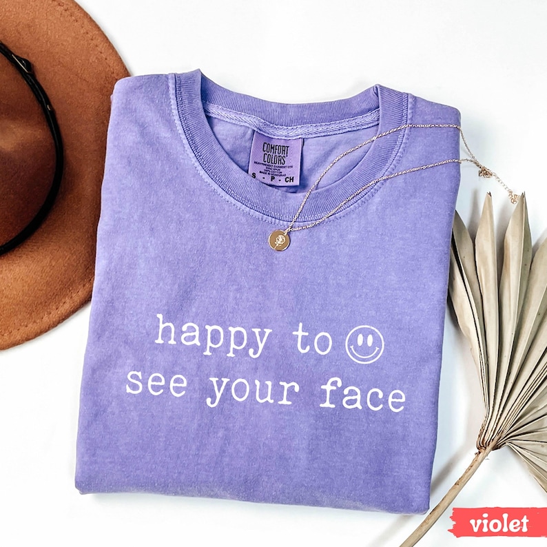 May include: A purple t-shirt with the text "happy to see your face" and a smiley face printed on the front.