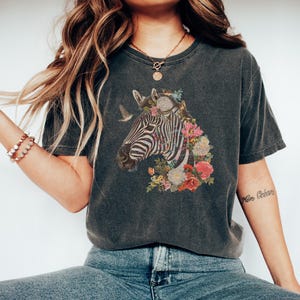 May include: A dark gray t-shirt with a graphic of a zebra's head surrounded by colorful flowers. The zebra has black and white stripes.
