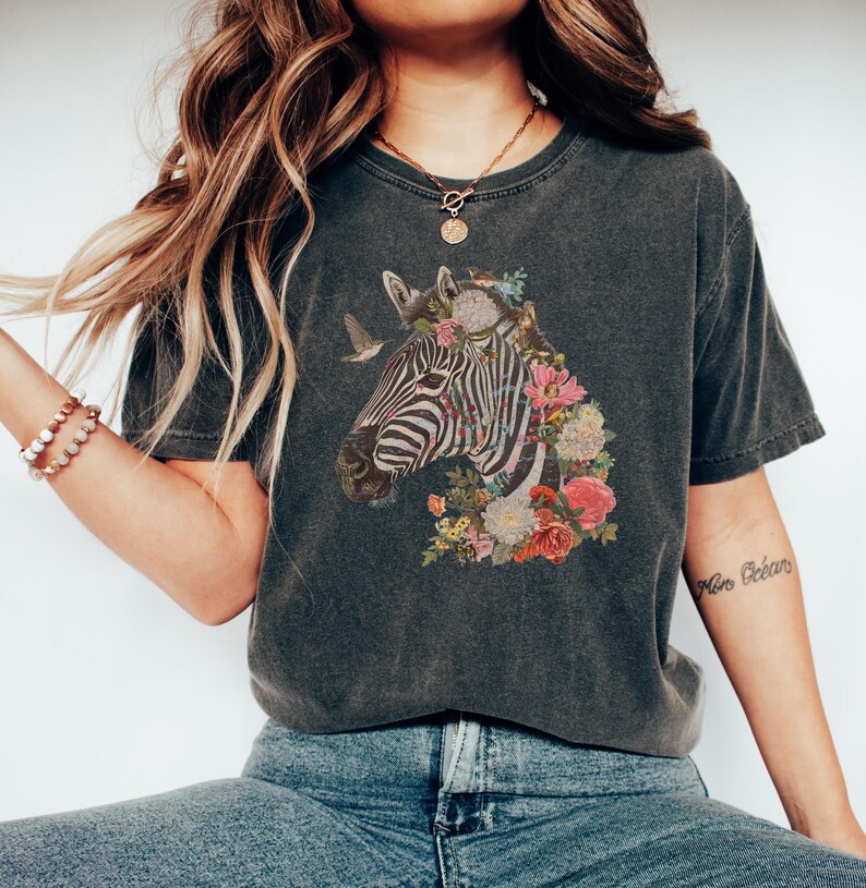 May include: A dark gray t-shirt with a graphic of a zebra's head surrounded by colorful flowers. The zebra has black and white stripes.