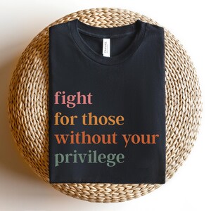 Op de afbeelding: Zwart T-shirt met de tekst "fight for those without your privilege" in kleurrijke letters.