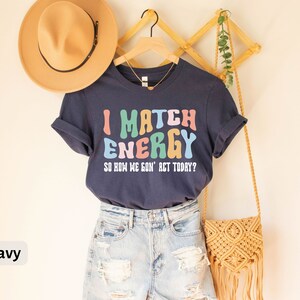 May include: Navy blue t-shirt with the text "I Match Energy So How We Gon' Act Today?" in colorful, wavy letters.