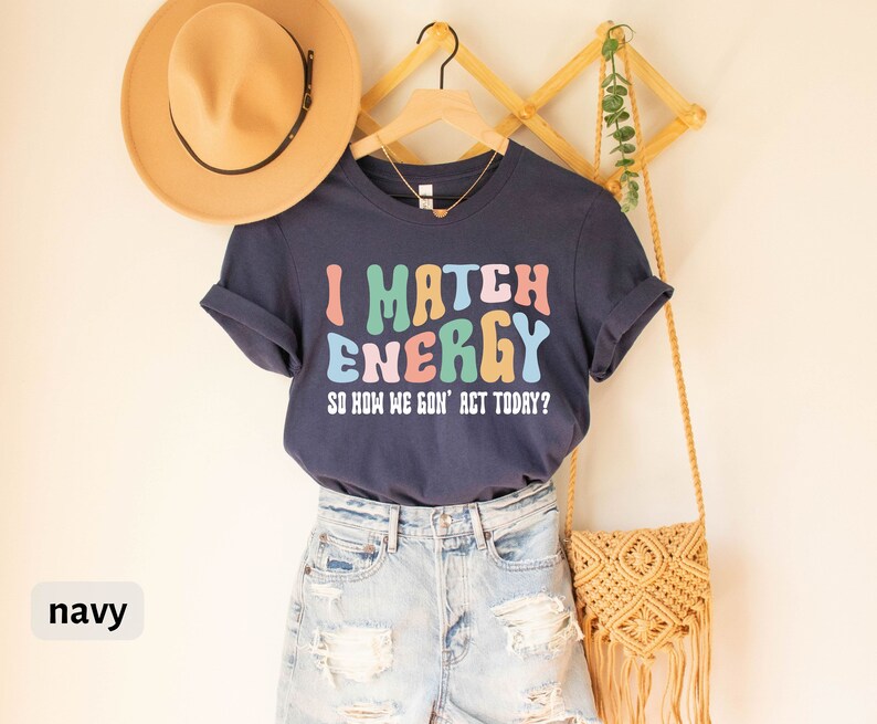 May include: Navy blue t-shirt with the text "I Match Energy So How We Gon' Act Today?" in colorful, wavy letters.
