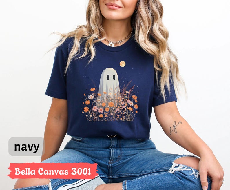 Pu&ograve; includere: T-shirt blu navy con un fantasioso disegno di un fantasma in mezzo a un campo di fiori sotto la luna piena. Il fantasma ha due occhi ovali neri. Il testo "navy" e "Bella Canvas 3001" sono visibili nell'immagine.
