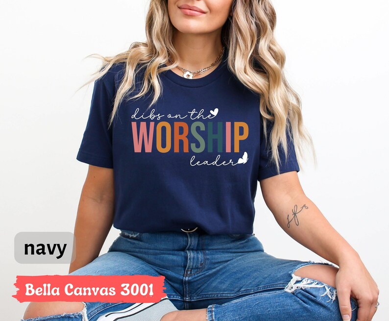 Puede incluir: Una camiseta azul marino con el texto "Dibs on the Worship Leader" en colores arco&iacute;ris y mariposas blancas. La camiseta est&aacute; hecha por Bella Canvas y es un estilo 3001.