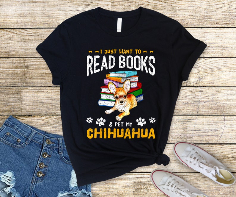 May include: Black t-shirt with a chihuahua sitting on a stack of books. The text on the shirt reads "I just want to read books & pet my chihuahua".