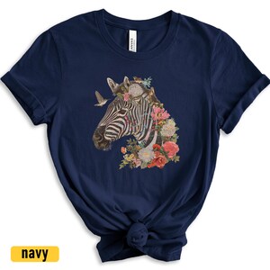 May include: A navy blue t-shirt with a graphic of a zebra's head adorned with colorful flowers. The zebra has black and white stripes and is surrounded by a variety of flowers in shades of pink, red, yellow, and purple.