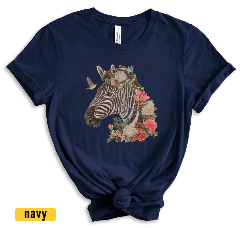 May include: A navy blue t-shirt with a graphic of a zebra's head adorned with colorful flowers. The zebra has black and white stripes and is surrounded by a variety of flowers in shades of pink, red, yellow, and purple.