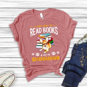 May include: A pink t-shirt with the text "I just want to read books & pet my chihuahua" in a distressed font. A chihuahua is sitting on top of a stack of books. The chihuahua is brown and white with floppy ears.
