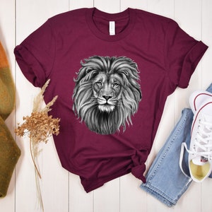 Może przedstawiać: Bordowy t-shirt z czarno-białym nadrukiem głowy lwa.