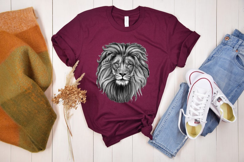 Może przedstawiać: Bordowy t-shirt z czarno-białym nadrukiem głowy lwa.