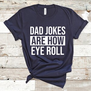 May include: A navy blue t-shirt with white text that reads "Dad Jokes Are How Eye Roll".