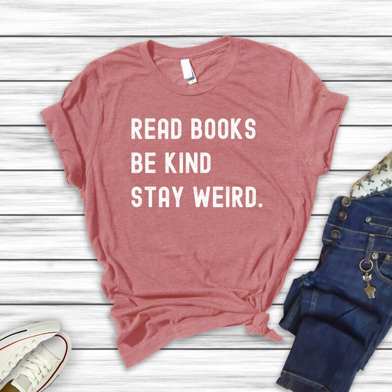 May include: A red heather t-shirt with the text "Read Books Be Kind Stay Weird." printed in white.