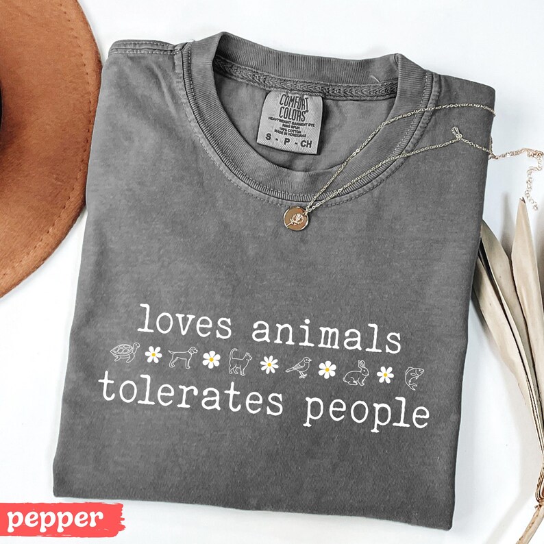 May include: A gray t-shirt with the text "loves animals tolerates people" in white. The text is surrounded by small white drawings of animals and flowers.