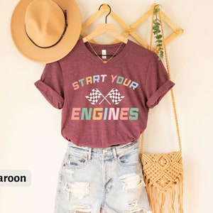 May include: Maroon t-shirt with the text "Start Your Engines" in rainbow colors and a checkered flag graphic.