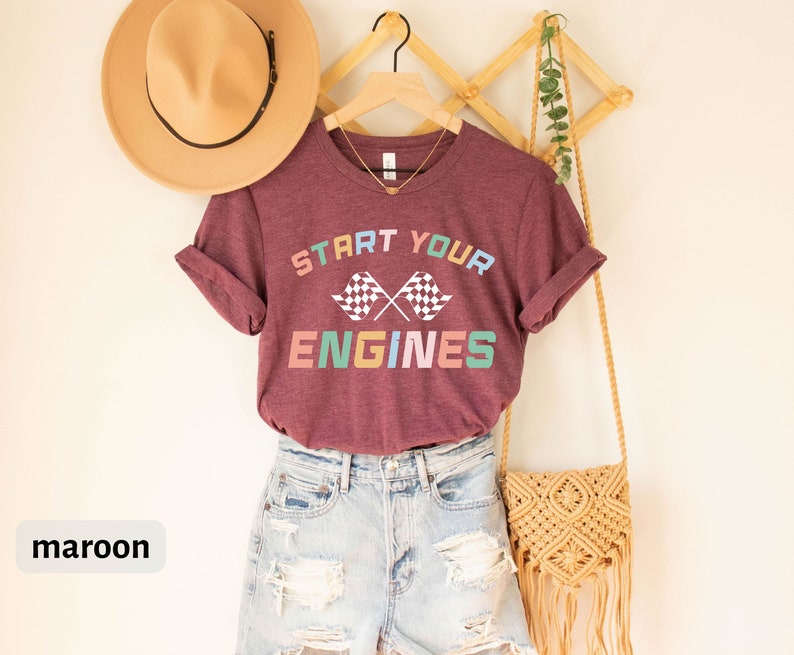 May include: Maroon t-shirt with the text "Start Your Engines" in rainbow colors and a checkered flag graphic.