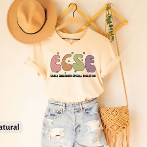 K&ouml;nnte beinhalten: Ein naturfarbenes T-Shirt mit dem Text "ECSE" in bunten, stilisierten Buchstaben. Der Text ist ein Akronym f&uuml;r "Early Childhood Special Education".