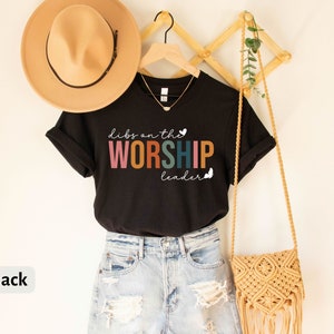 Puede incluir: Camiseta negra con el texto "Dibs on the Worship Leader" en colores arco&iacute;ris y un peque&ntilde;o coraz&oacute;n y una mariposa.