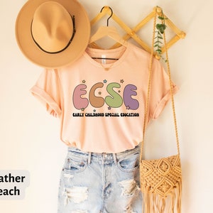 K&ouml;nnte beinhalten: T-Shirt in der Farbe Heide-Pfirsich mit einer Grafik der Buchstaben "ECSE" in bunten, abgerundeten Formen mit Sternen. Der Text "EARLY CHILDHOOD SPECIAL EDUCATION" befindet sich unter der Grafik.