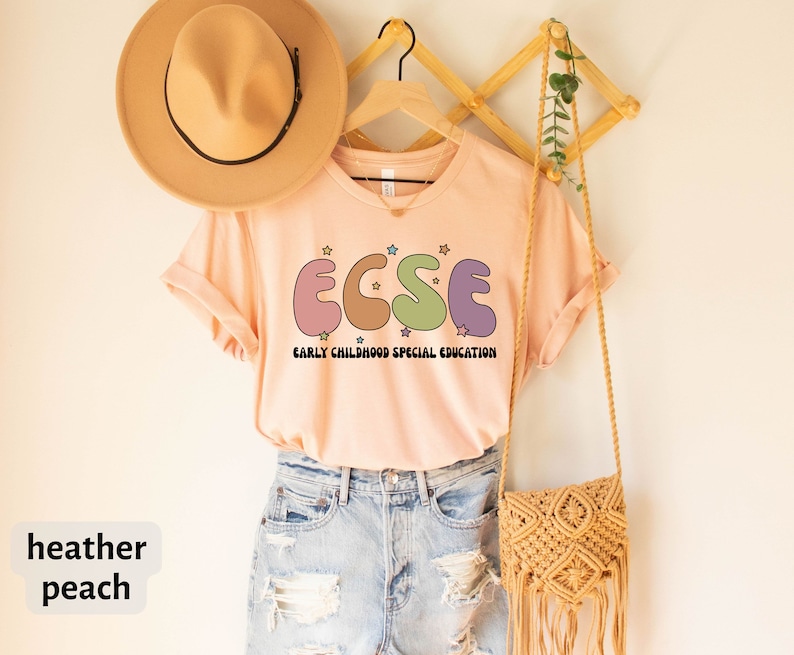 K&ouml;nnte beinhalten: T-Shirt in der Farbe Heide-Pfirsich mit einer Grafik der Buchstaben "ECSE" in bunten, abgerundeten Formen mit Sternen. Der Text "EARLY CHILDHOOD SPECIAL EDUCATION" befindet sich unter der Grafik.
