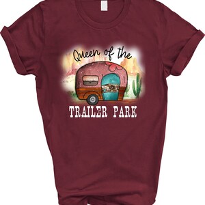 May include: A maroon t-shirt with a graphic of a vintage camper in a desert landscape. The text "Queen of the Trailer Park" is printed below the camper.