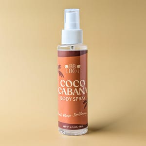 Puede incluir: Un frasco transparente de spray corporal con un pulverizador blanco. La etiqueta es marr&oacute;n con las palabras "COCO CABANA BODY SPRAY" y "Beach Please - I'm Glowing". El frasco contiene 118 ml de producto.