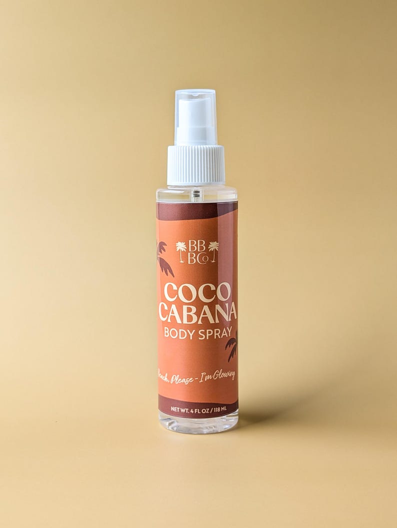 Puede incluir: Un frasco transparente de spray corporal con un pulverizador blanco. La etiqueta es marr&oacute;n con las palabras "COCO CABANA BODY SPRAY" y "Beach Please - I'm Glowing". El frasco contiene 118 ml de producto.