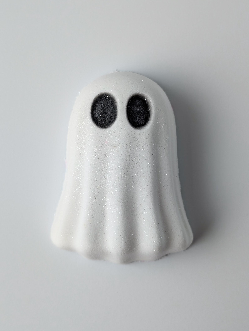 May include: A white, ghost-shaped item with two black, circular eyes. The ghost has a textured, glittery surface. The design is simple and evokes a Halloween theme.