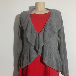 May include: Gray cardigan with a ruffled front and long sleeves. The cardigan is draped over a red dress.