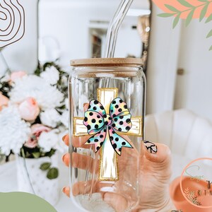 May include: A clear glass tumbler with a bamboo lid and a straw. The tumbler has a colorful bow and cross design on it.